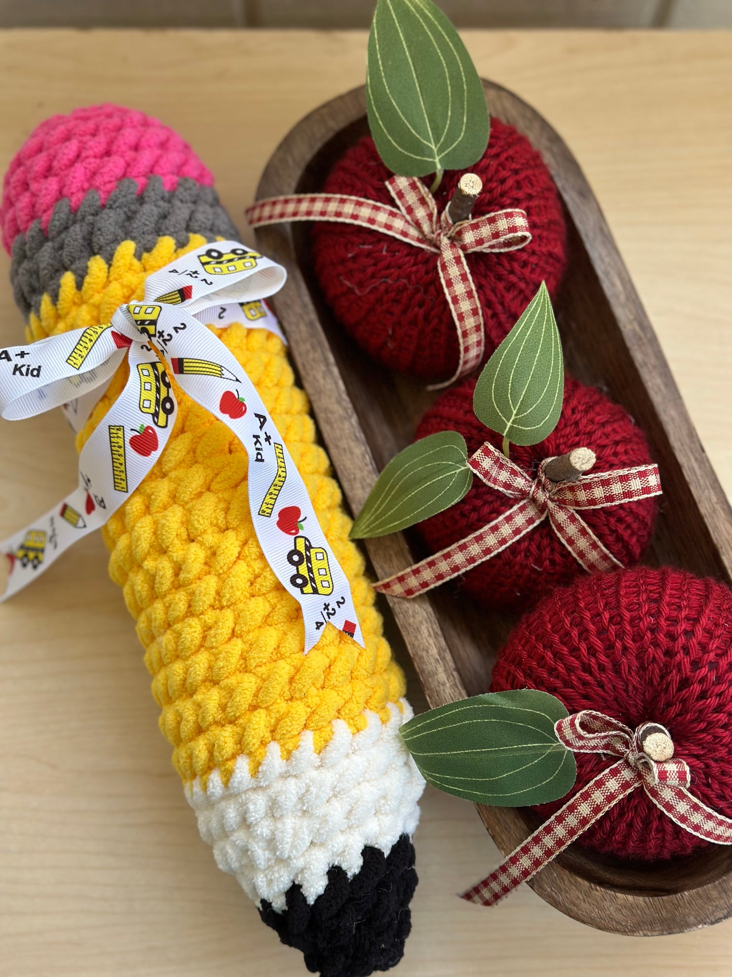 Crocheted pencil and apples with ribbons on a wooden surface
