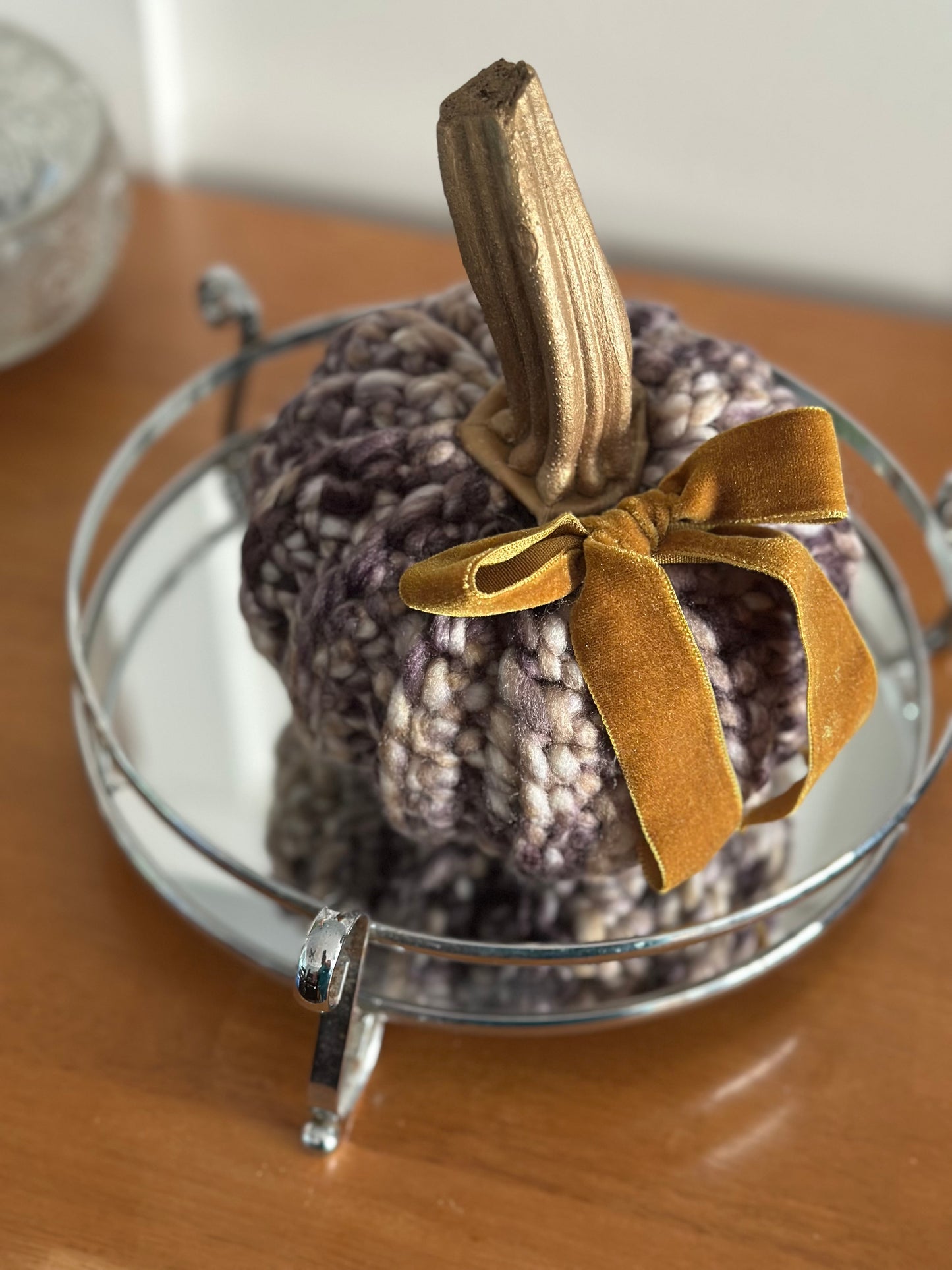 crochet pumpkin with a natural painted stem and gold velvet ribbon on a mirrored stand.