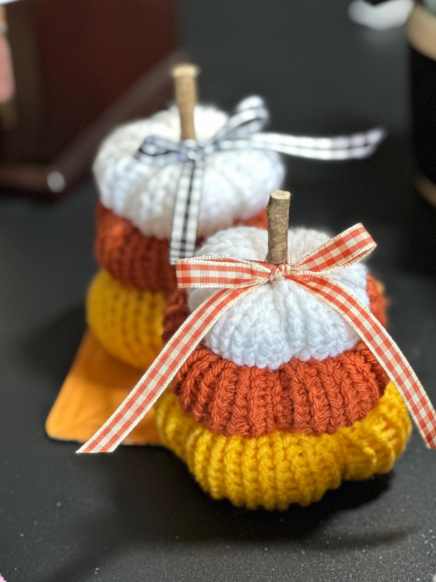 Knitted pumpkins in white, orange, and yellow with ribbons on a dark surface