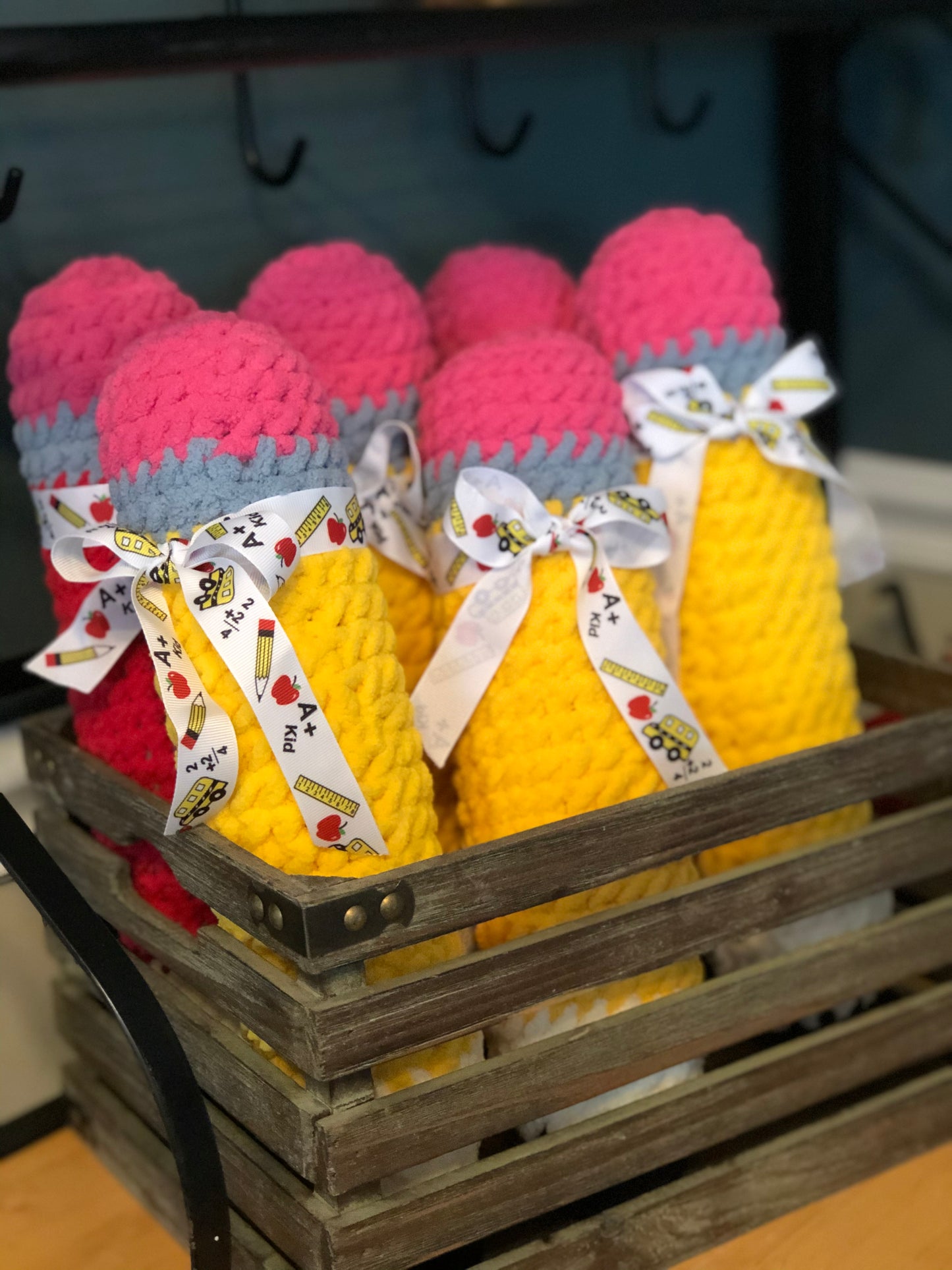 Crocheted pencils in pink and yellow with ribbons in a wooden crate.