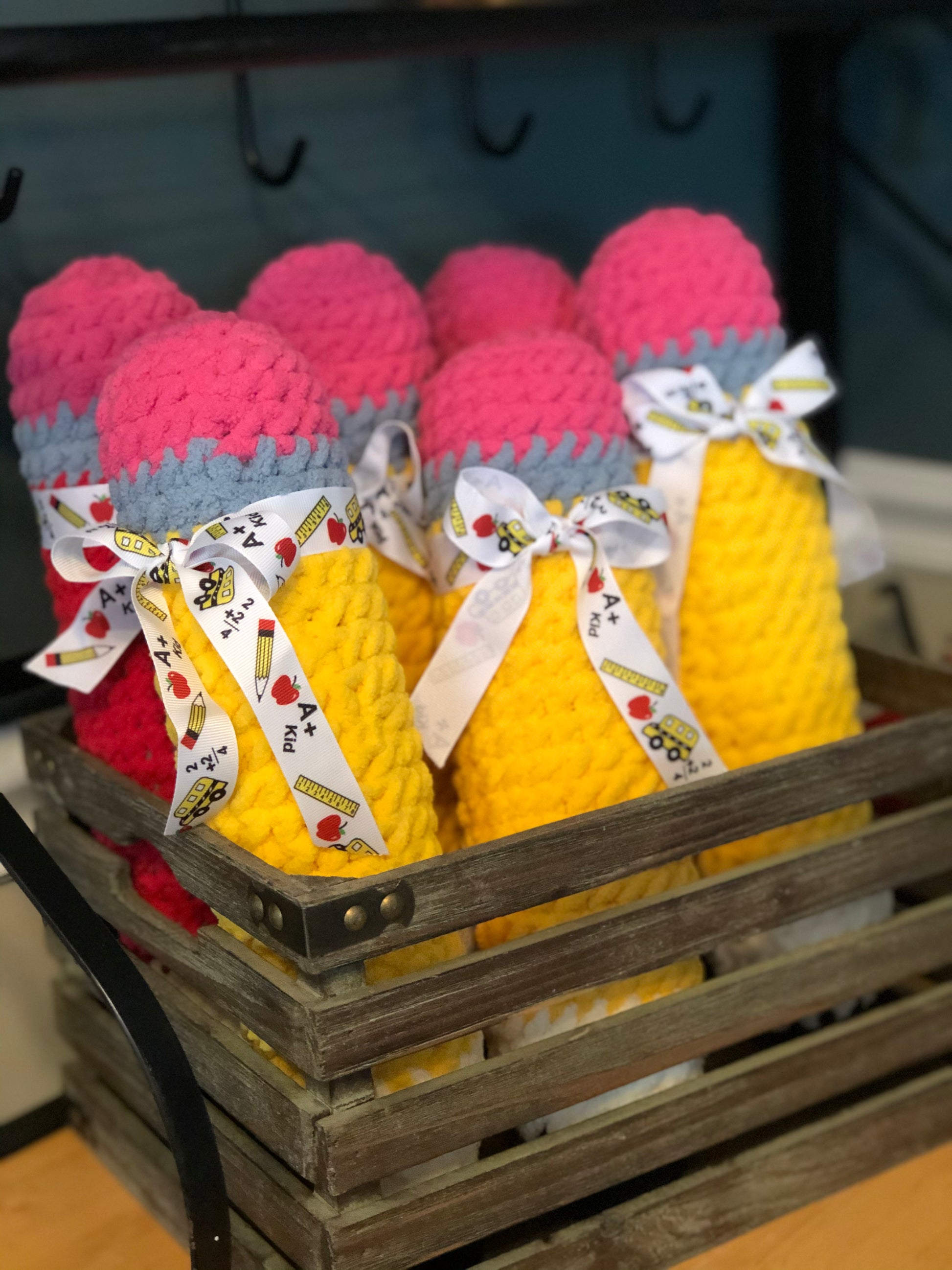 Crocheted pencils in pink and yellow with ribbons in a wooden crate.