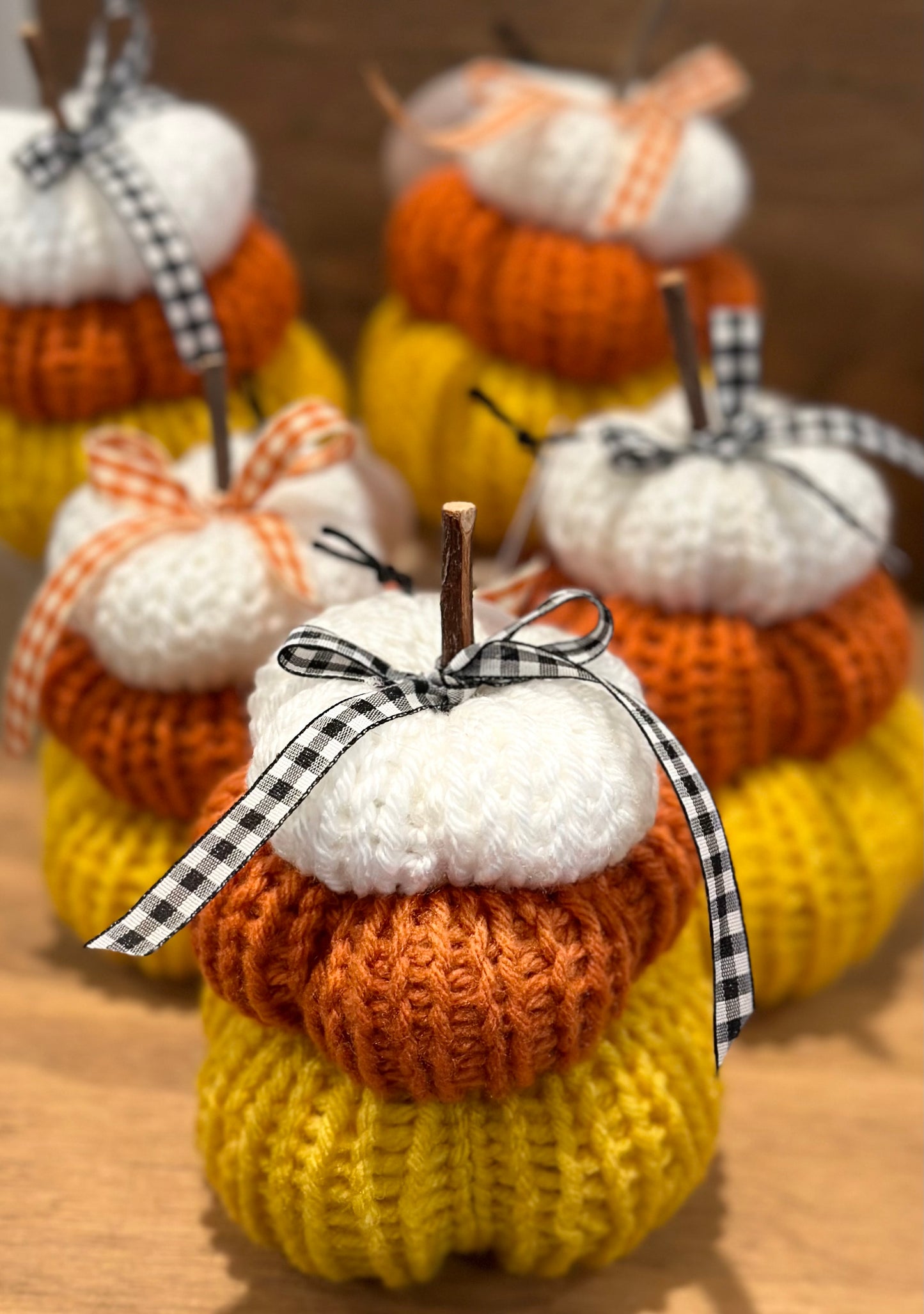 Knitted pumpkins in orange, white, and yellow with checkered ribbons on a wooden surface.