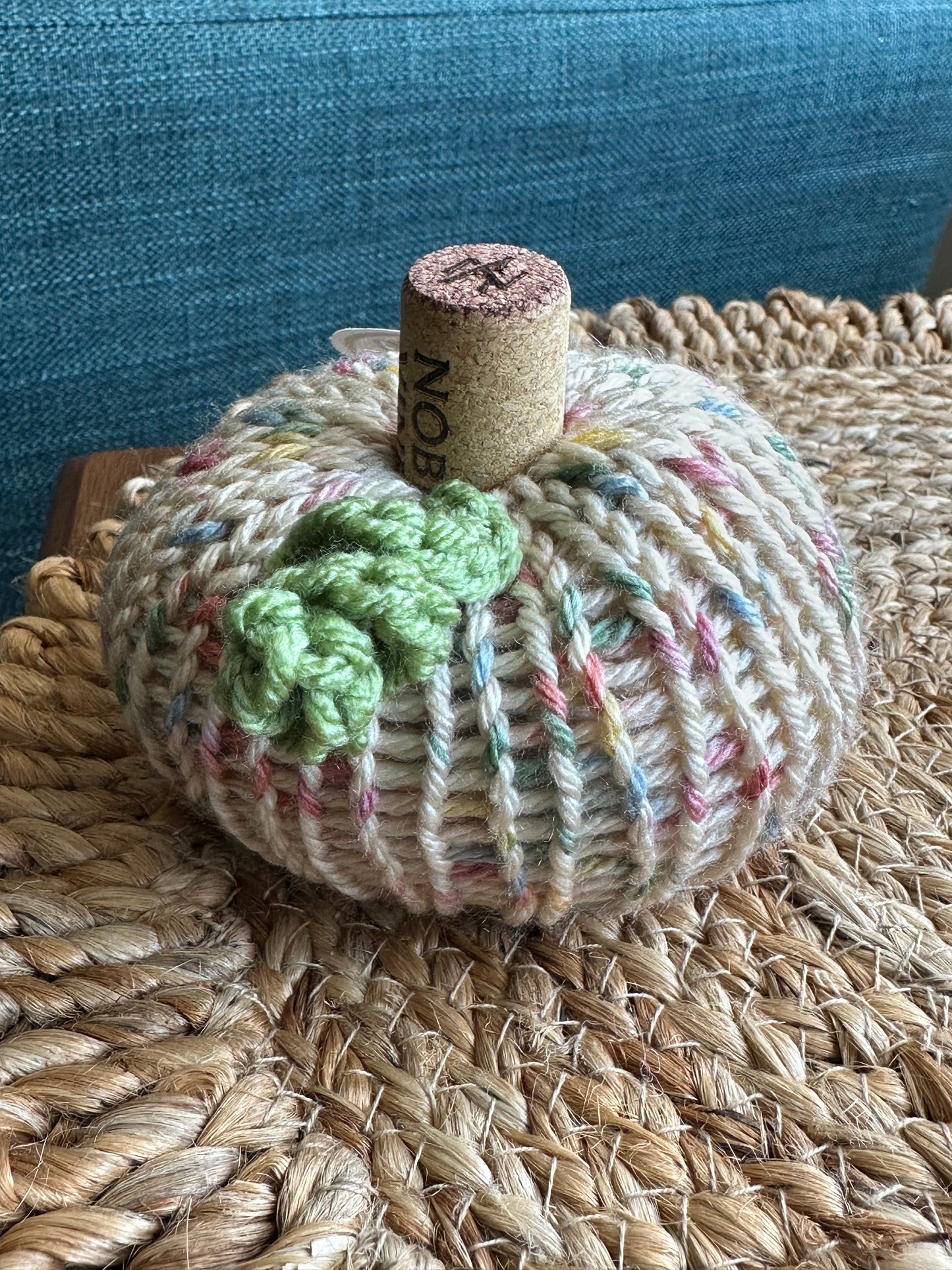 Knitted yarn pumpkin with a green crochet tendril on a woven surface