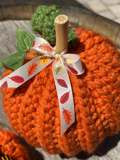 crocheted wool pumpkin decoration with a leaf-patterned ribbon on a wooden surface