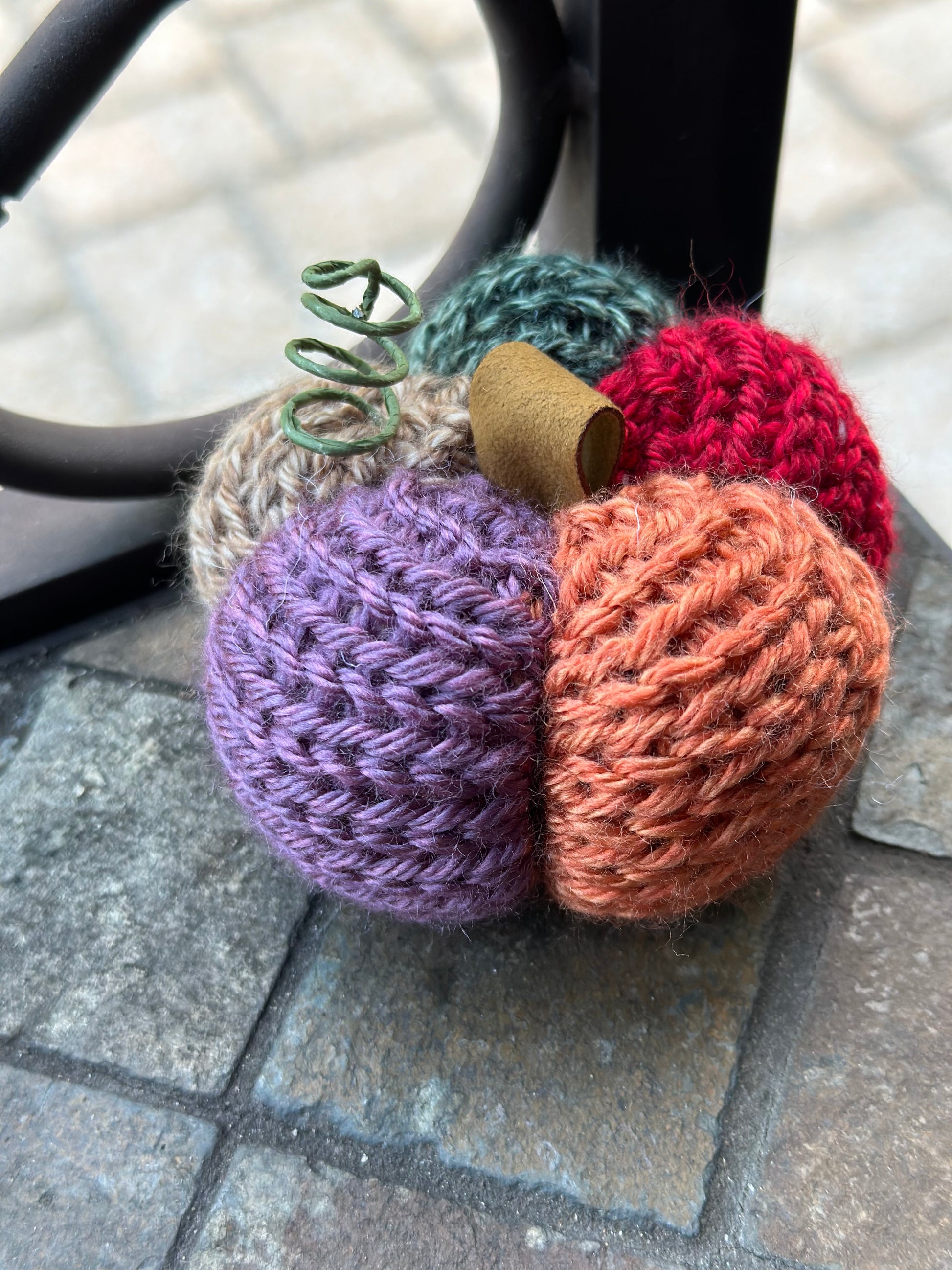 Colorful knitted flower-shaped pumpkin on a stone surface with trellis in back