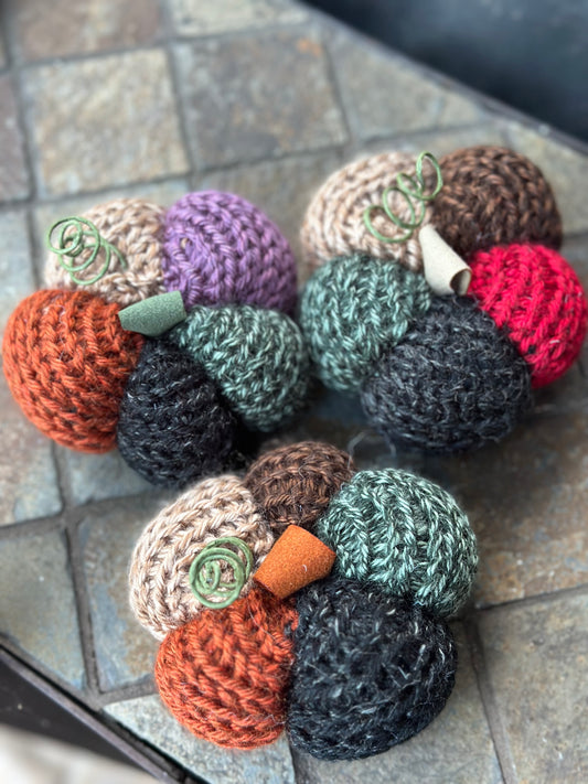 Collection of knit pumpkins in various colors on a stone surface