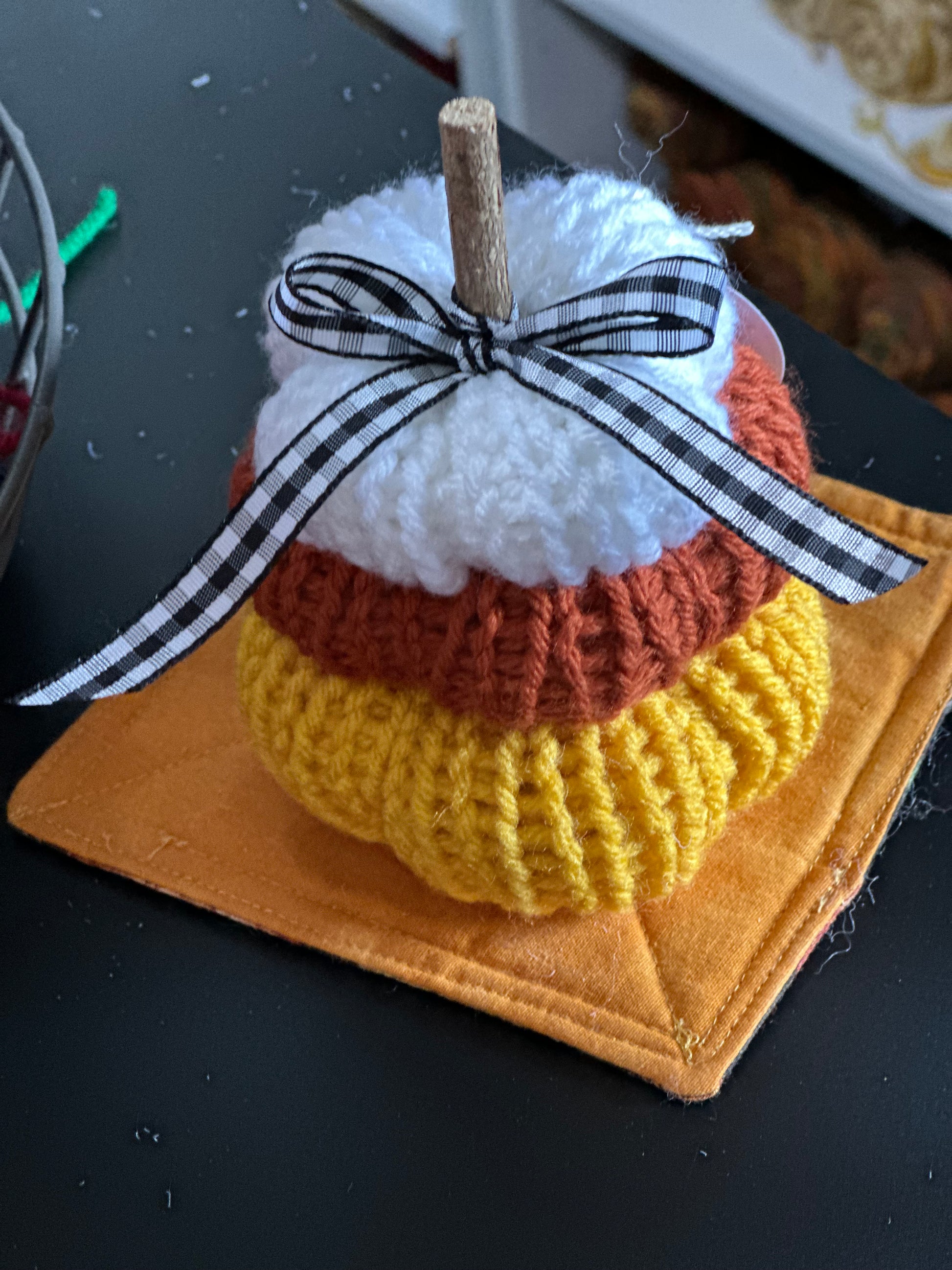 Stack of knit pumpkin in candy corn colors with a black and white plaid ribbon on a dark surface