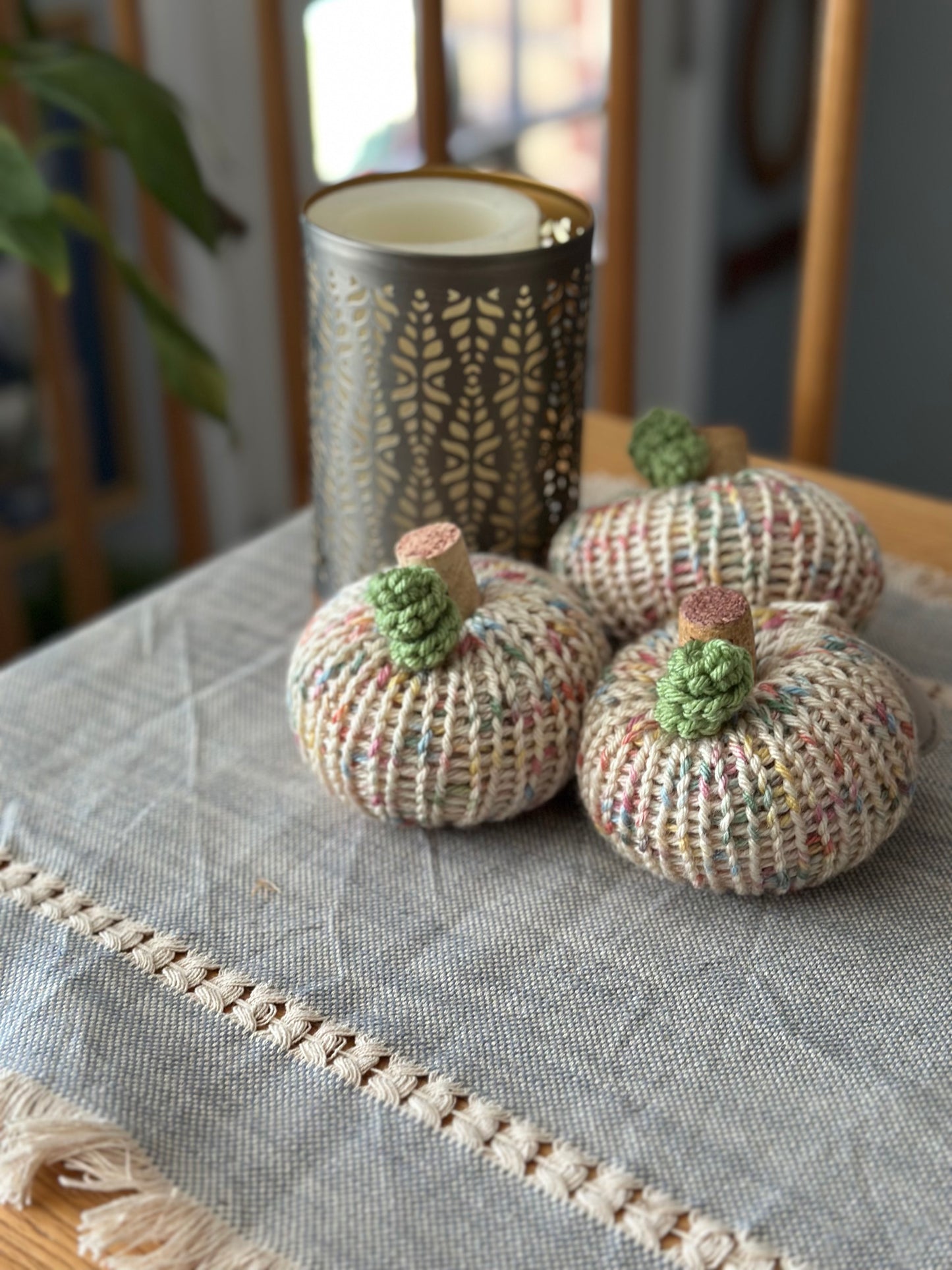 Three knitted pumpkins on a textured tablecloth with a decorative vase in the background.