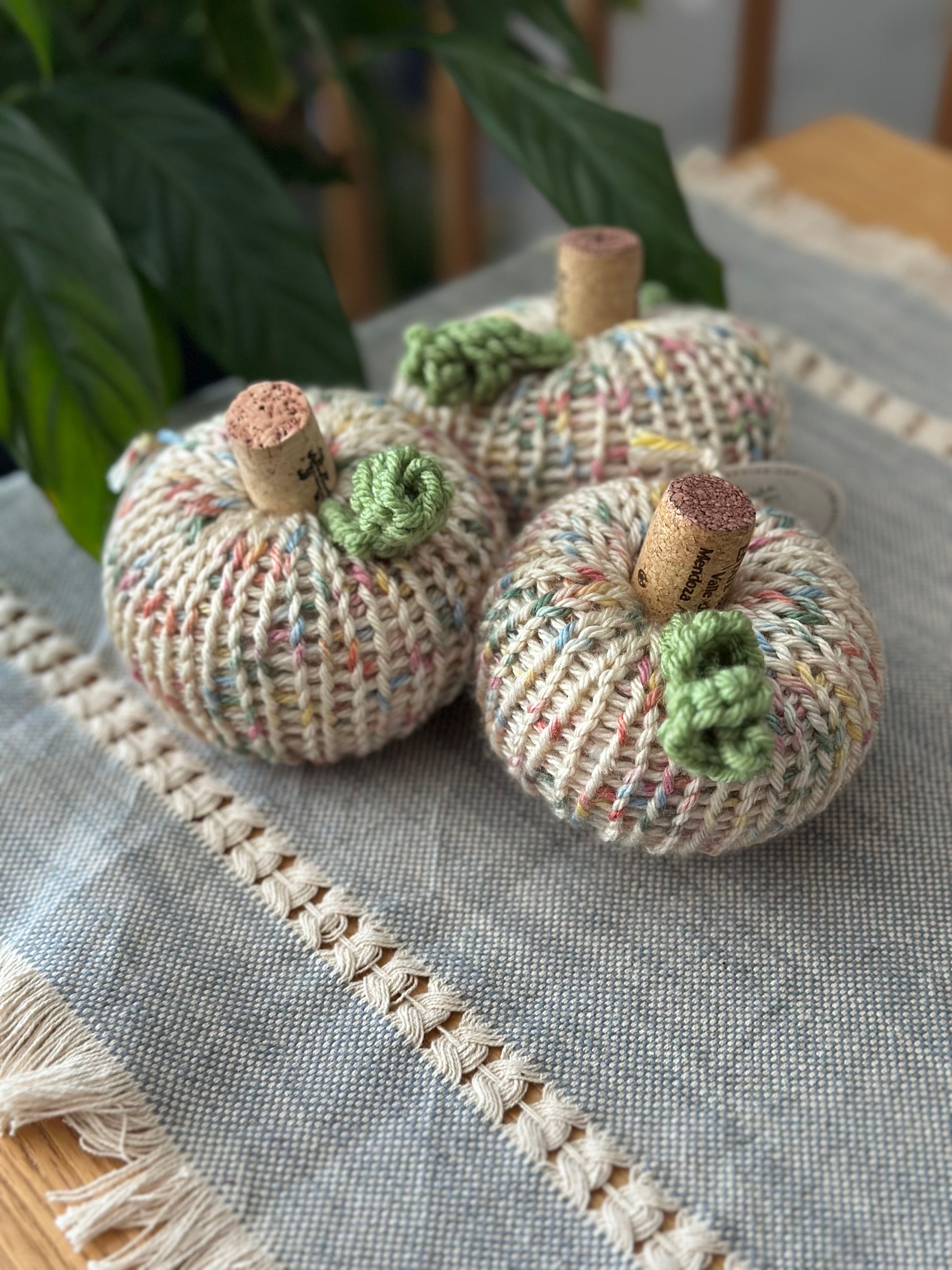 Three knitted pumpkins with cork stems on a textured surface.
