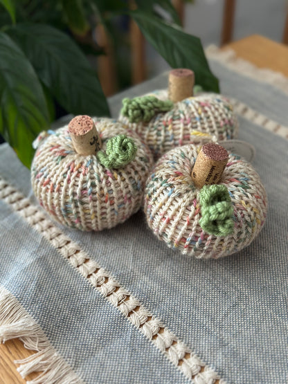 Three knitted pumpkins with cork stems on a textured surface.