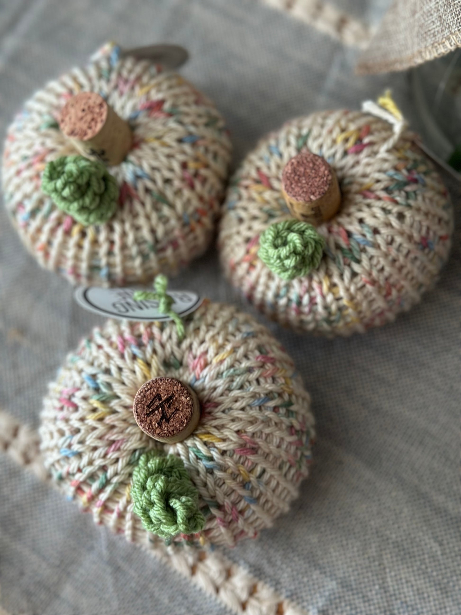Three knitted pumpkins with cork stems on a textured fabric background